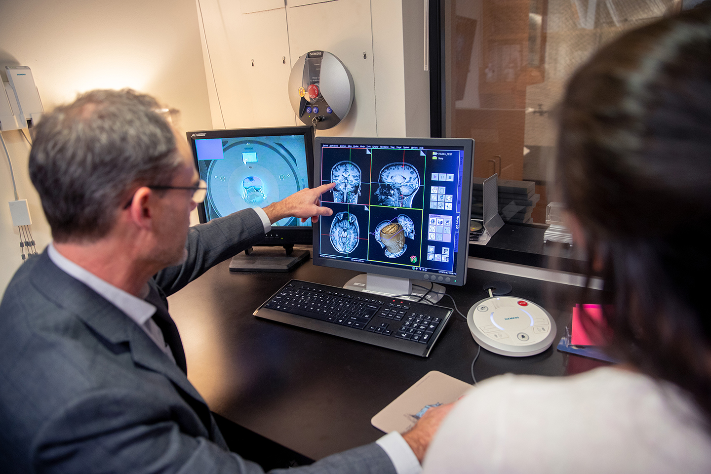 Man pointing at computer monitor displaying brain scans