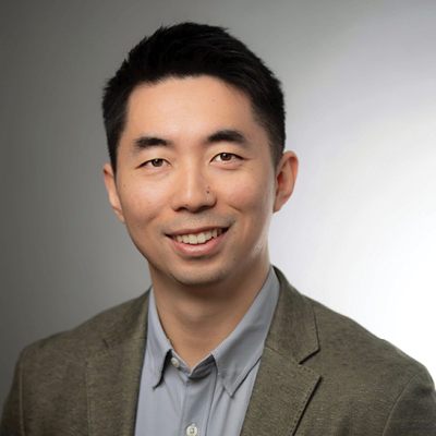 Asian man with short hair in a suit smiles for a portrait in front of a gray background